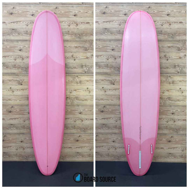 A pink surfboard displayed in two orientations on a wooden background, showing the top and bottom of the board.